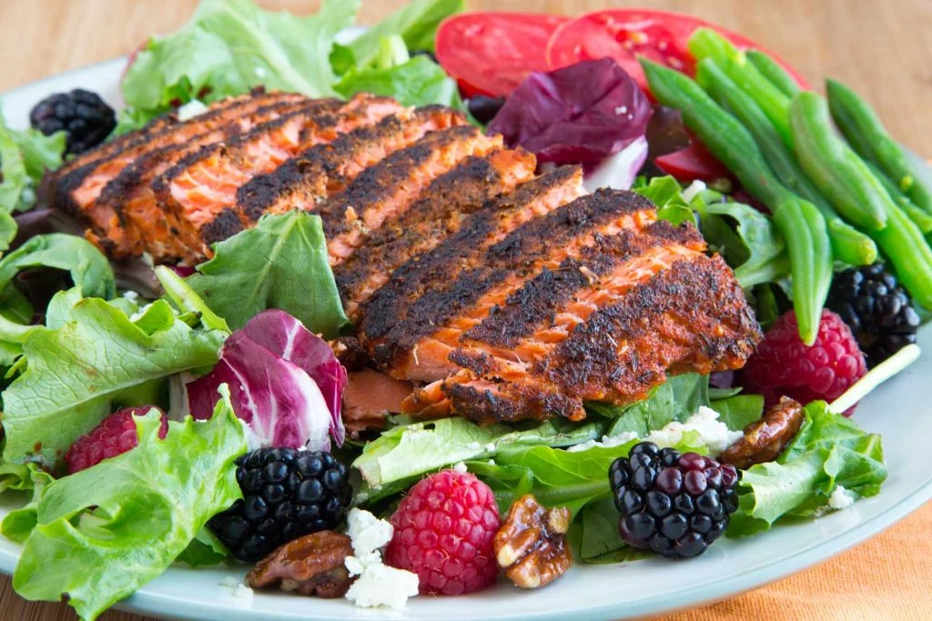 Blackened salmon on a bed of lettuce with tomatoes, green beans, and berries.