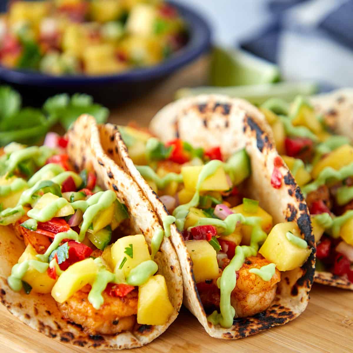 Shrimp tacos with mango salsa on a wooden cutting board.