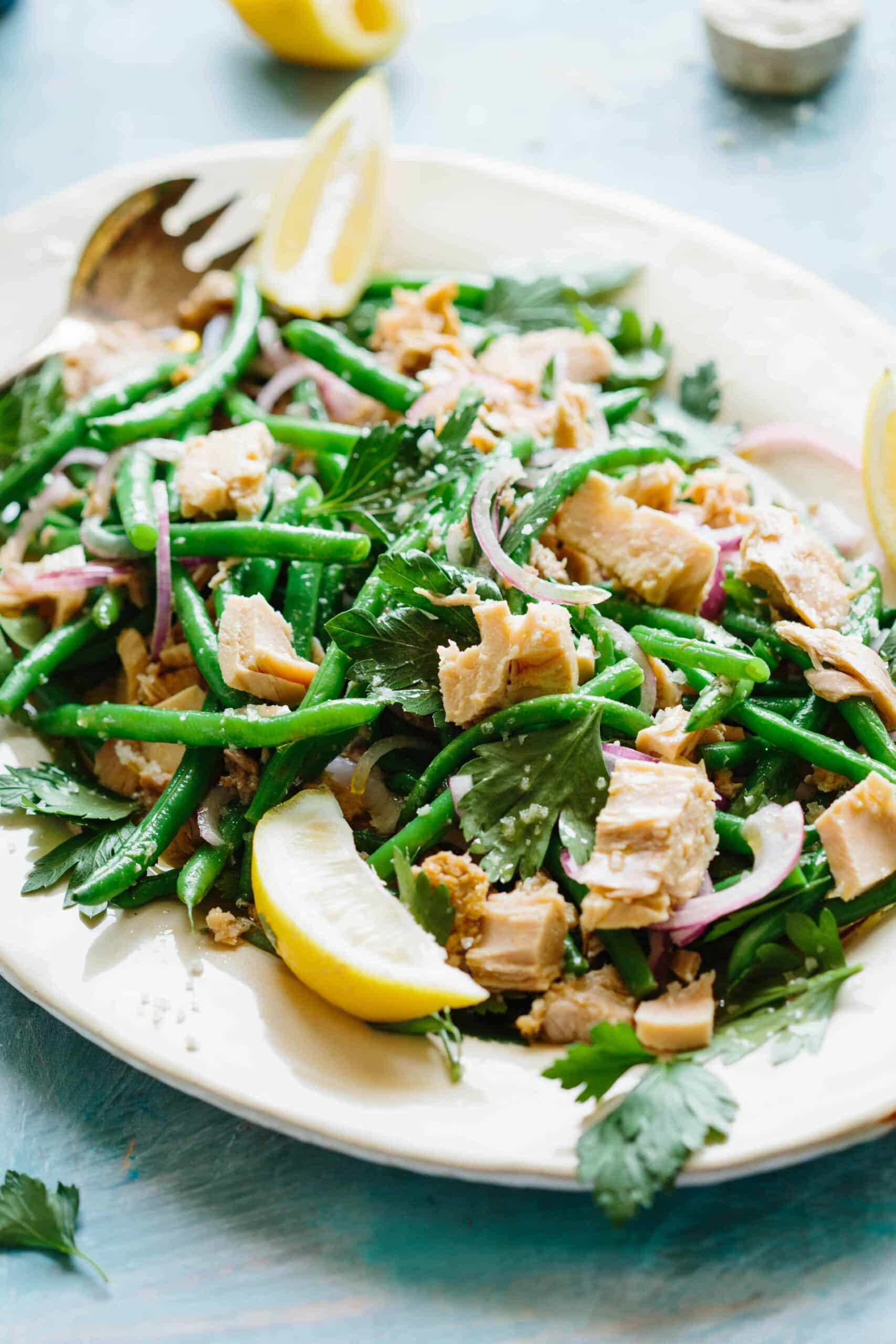 Italian tuna salad with green beans red onions, and lemon wedges on a plate.