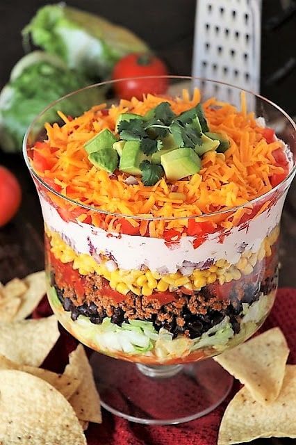 Layered taco salad in a bowl with lettuce, olives, ground beef, salsa, corn, sour cream, tomatoes, cheese, and avocado.