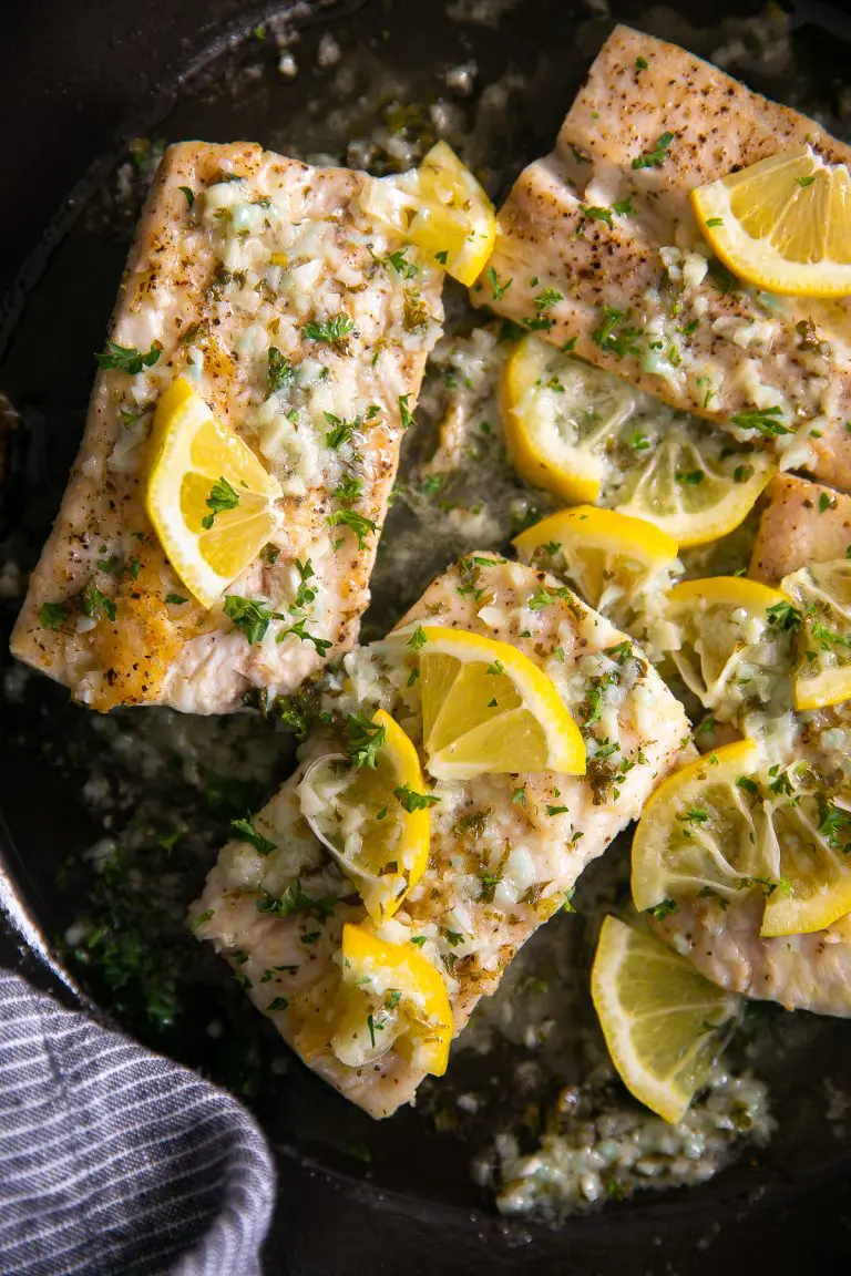 Mahi mahi with lemon garlic sauce in a pan with lemon wedges.