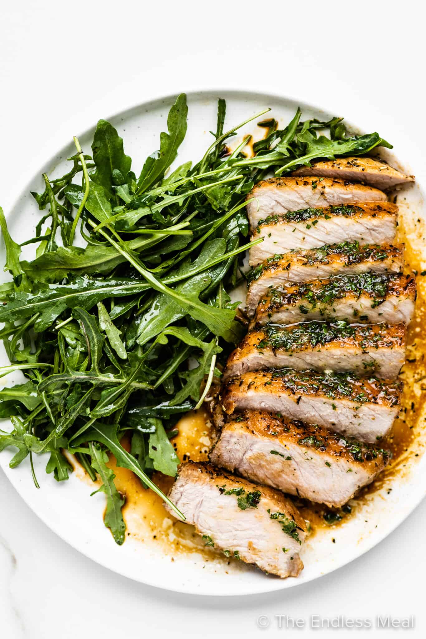 Sliced pan seared pork chops drizzled with honey herb butter and arugula salad.
