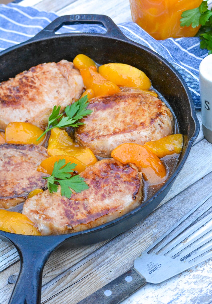 Pork chops and peaches in a cast iron pan.