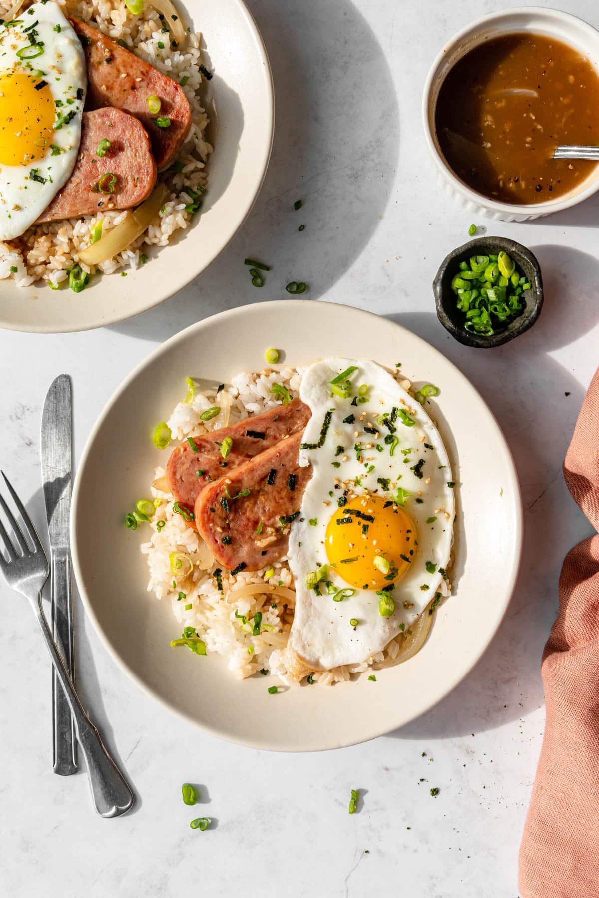 Lightly fried spam on a plate with furikake seasoned sunny side up eggs, and seasoned rice.