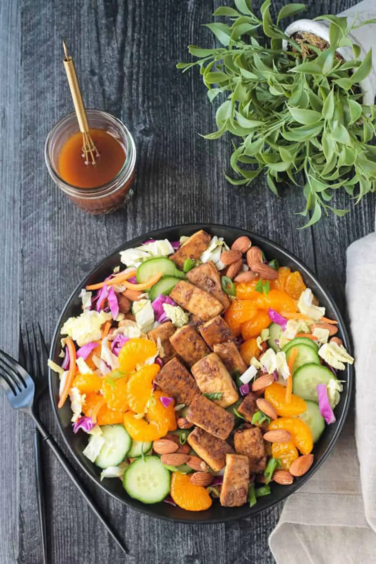 Chinese tofu salad with tofu, mandarin, cabbage, carrots, cucumber, almonds, with dressing and fork in the background.