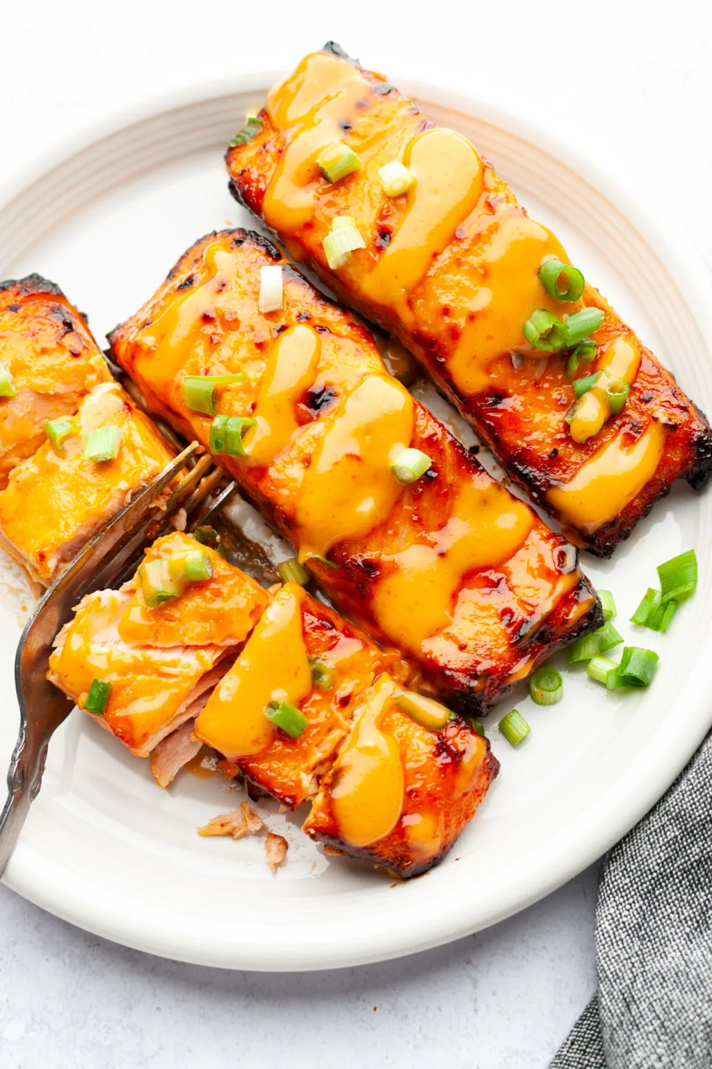 Salmon fillets with bang bang sauce on a white plate.