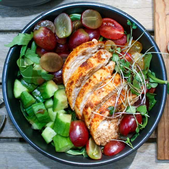 Sliced blackened chicken with cucumber, grapes, cucumber, and lettuce in a bowl.