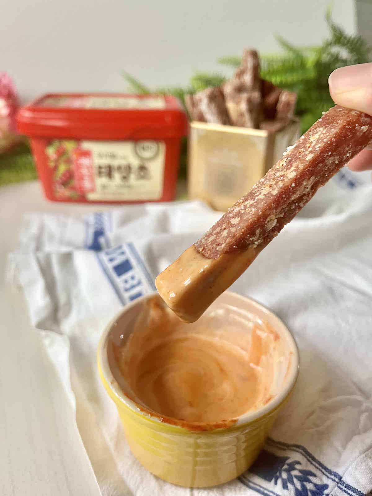 Spam fry held in hand dipping into gochujang mayo.