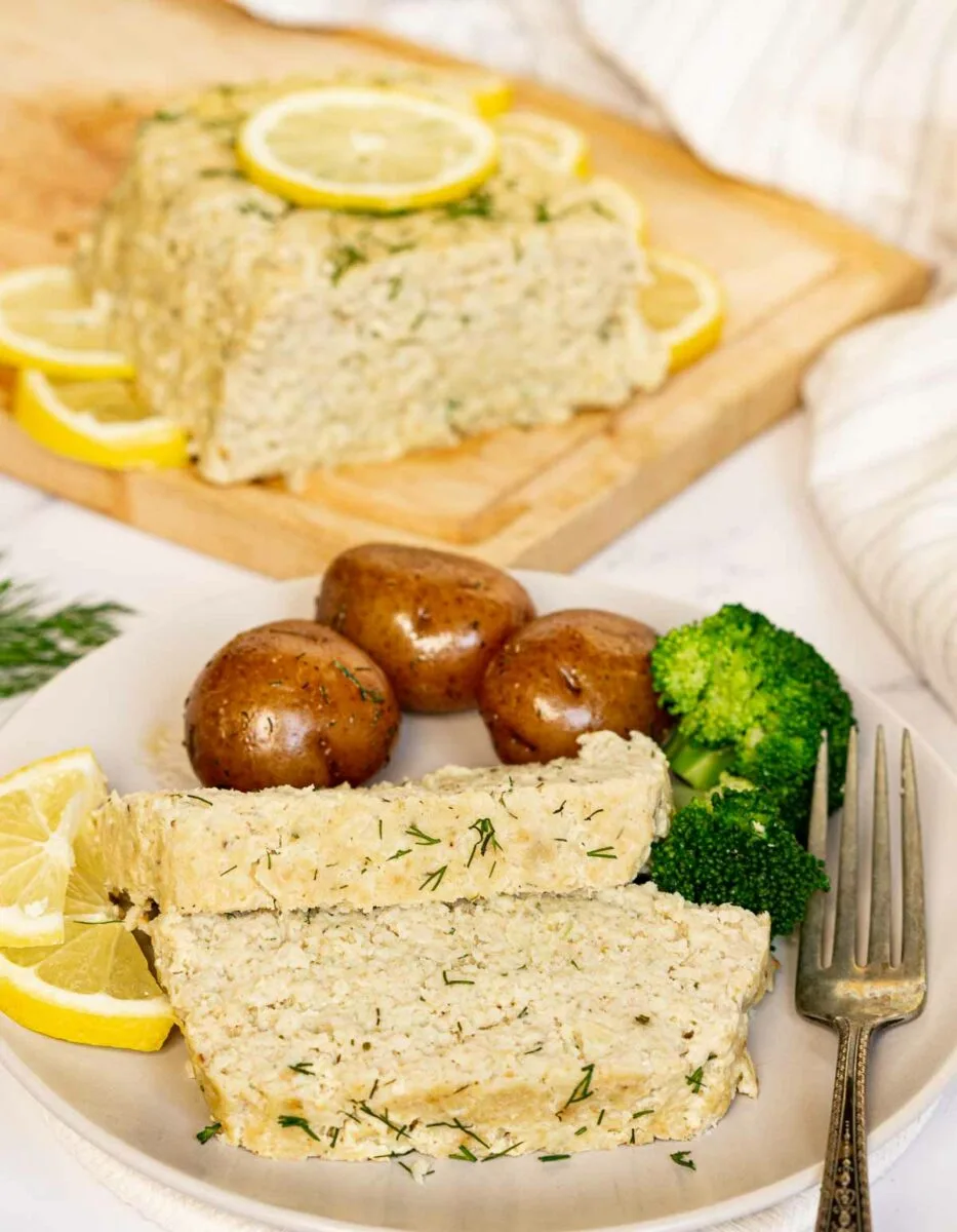 Fish loaf on a plate with lemon wedges, broccoli and potatoes.