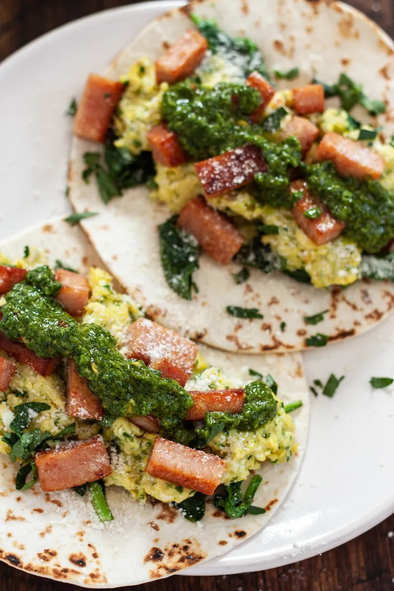 Green eggs and spam tacos with green sauce on a white plate.