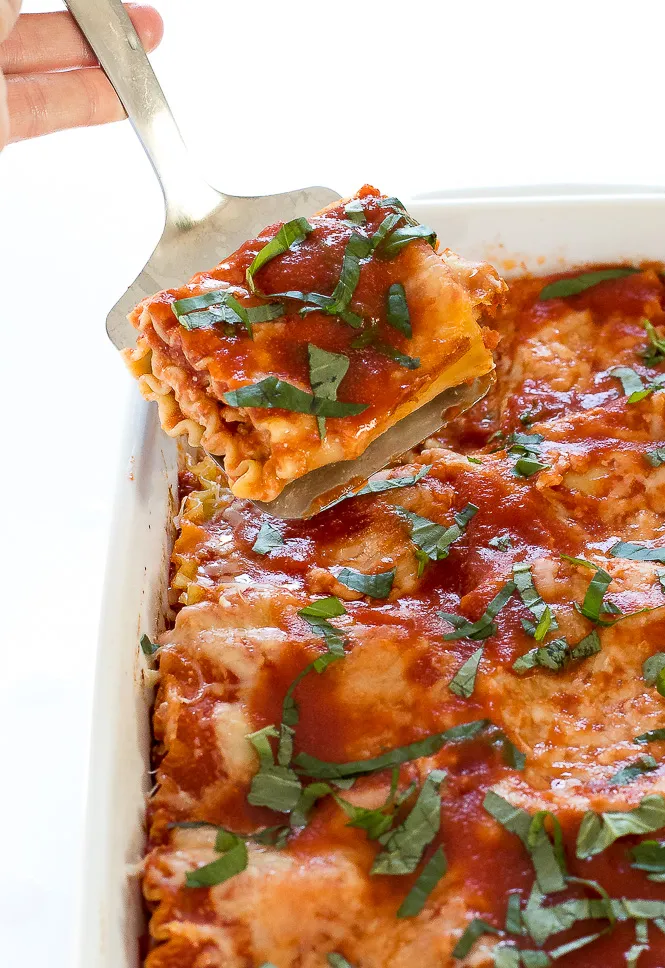 Hand holding spatula lifting lasagna roll up.