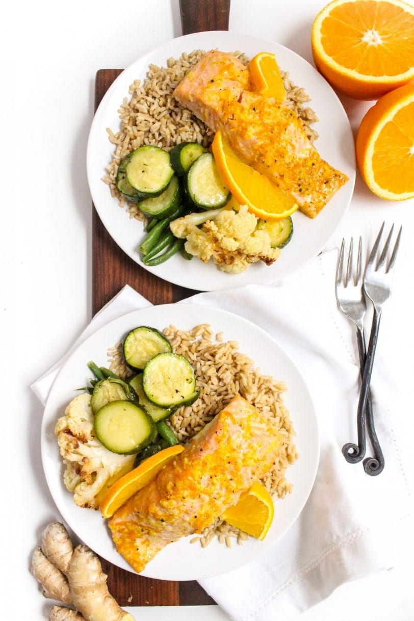 Orange ginger salmon recipe with rice and vegetables on plates with forks and napkins in the background.