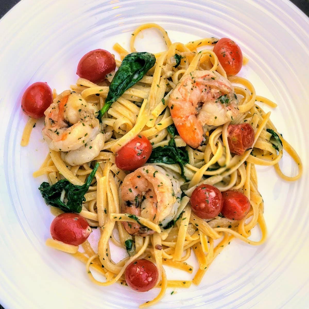 Garlic butter shrimp pasta with tomatoes and spinach on a white plate.