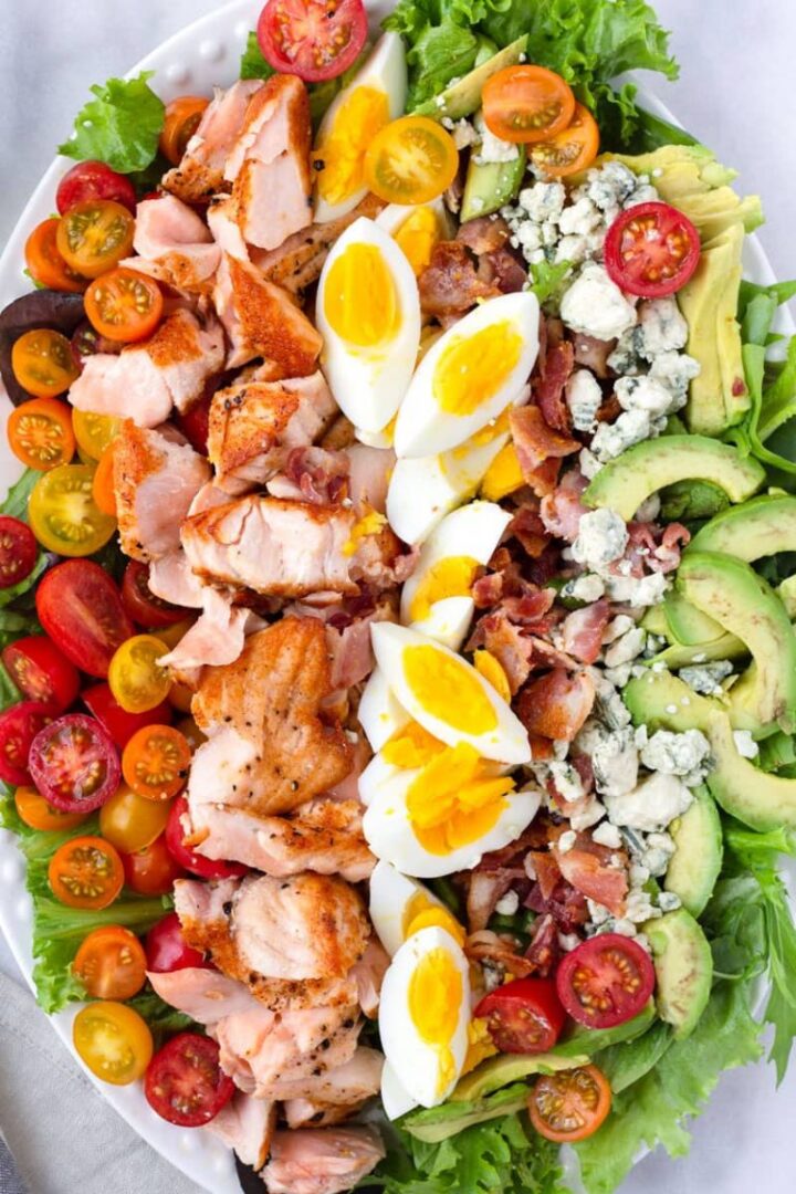 Salmon cobb salad with hard boiled eggs, tomatoes, bacon, blue cheese, lettuce, and avocado.