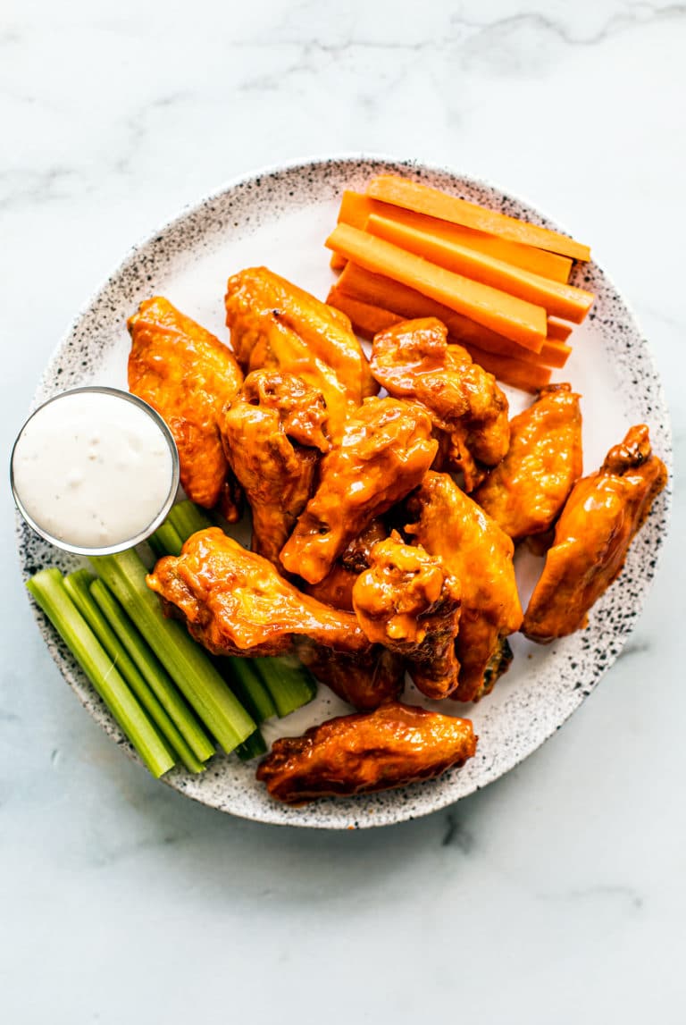Buffalo chicken wings with celery, carrots, and dipping sauce on a white plate.