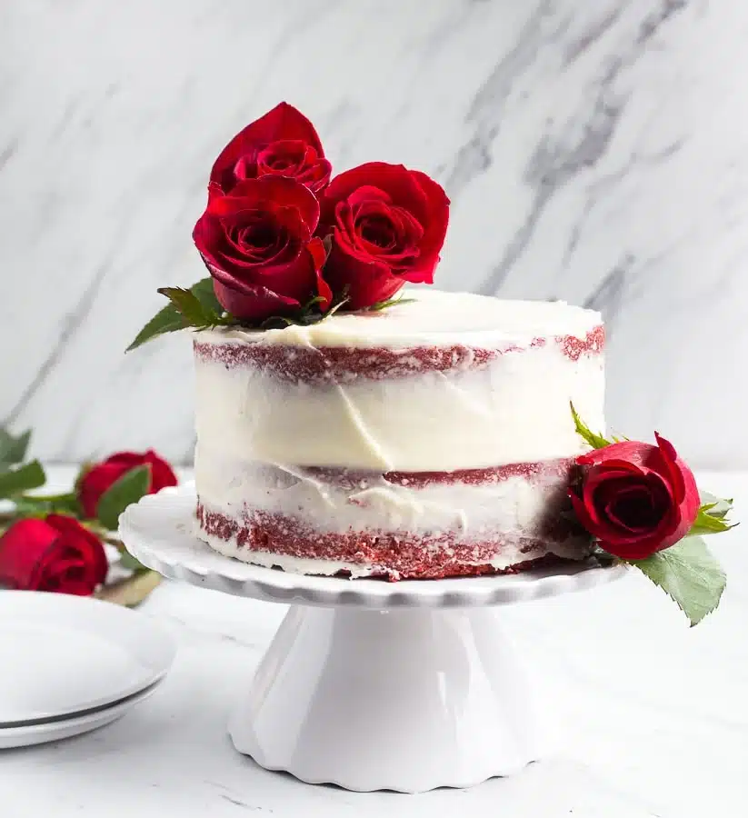 Mini red velvet cake on white cake stand with red roses.