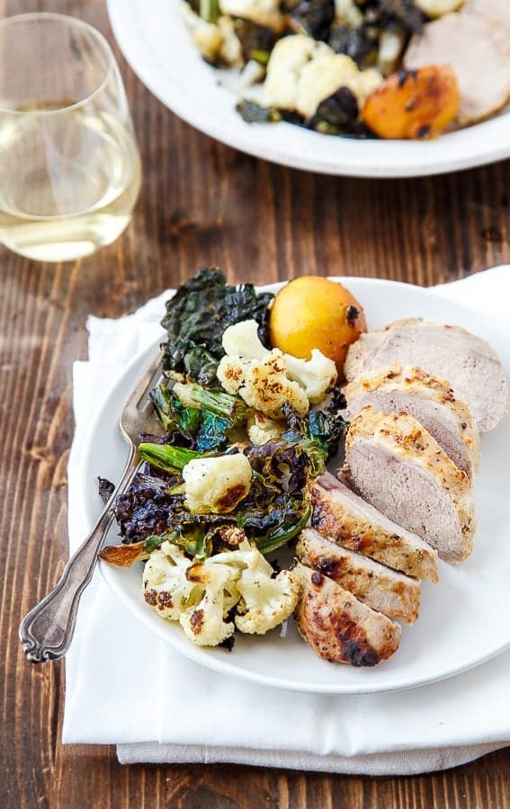 Slices of pork tenderloin, kale, and cauliflower with a fork on a white plate.