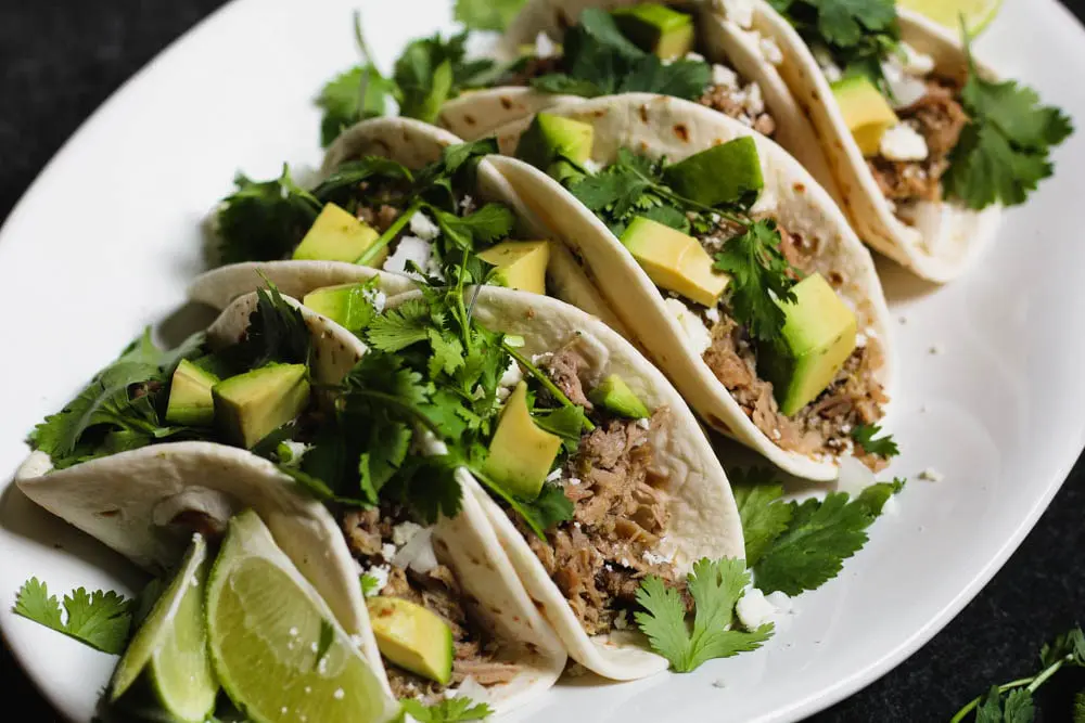 Braised salsa verde pork tacos on a white plate.