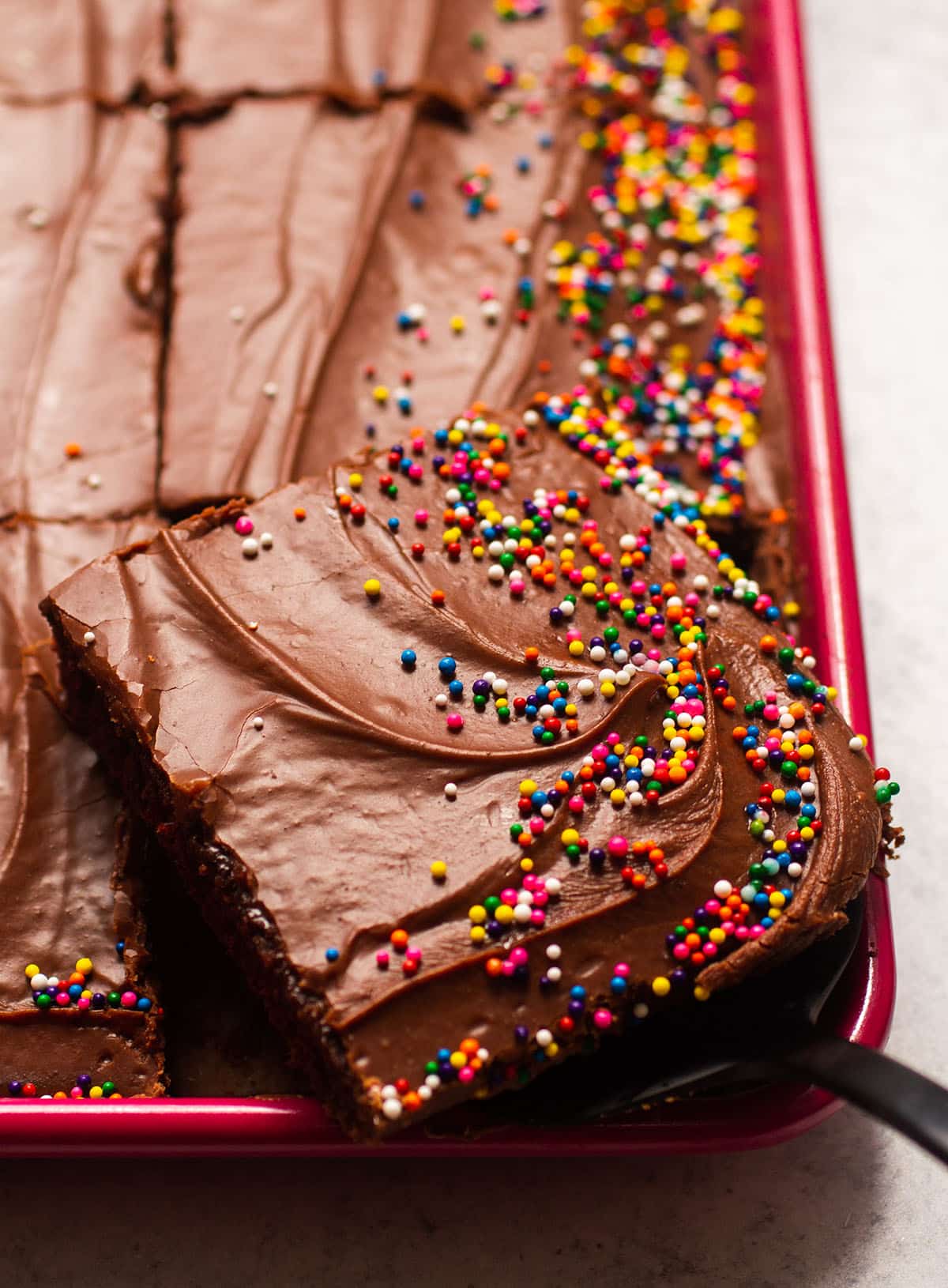 Slice of chocolate sheet cake with fudge frosting in a red baking dish.