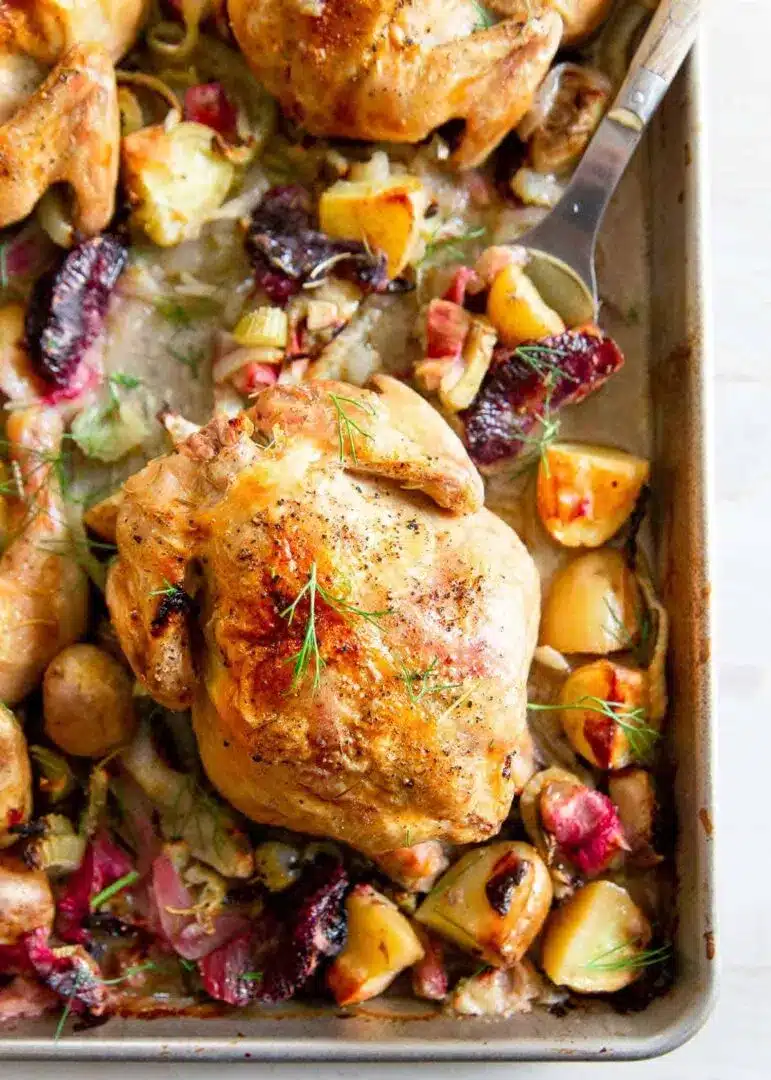 Cornish game hens with rhubarb, onions, and potatoes on a sheet pan.