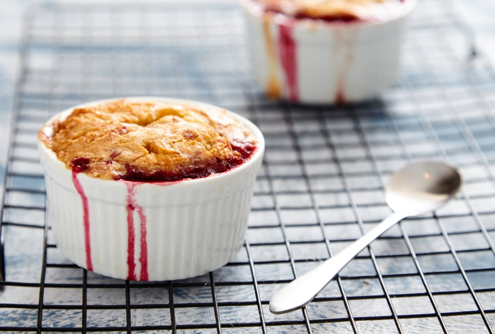 Individual cherry crumble in ramekins on a cooling rack.