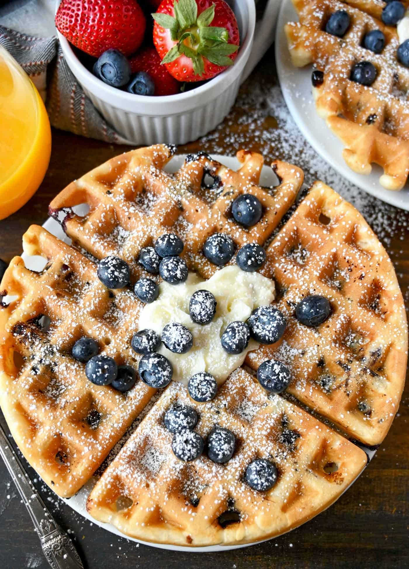 Blueberry waffles with whipped cream, blueberries, and powdered sugar.
