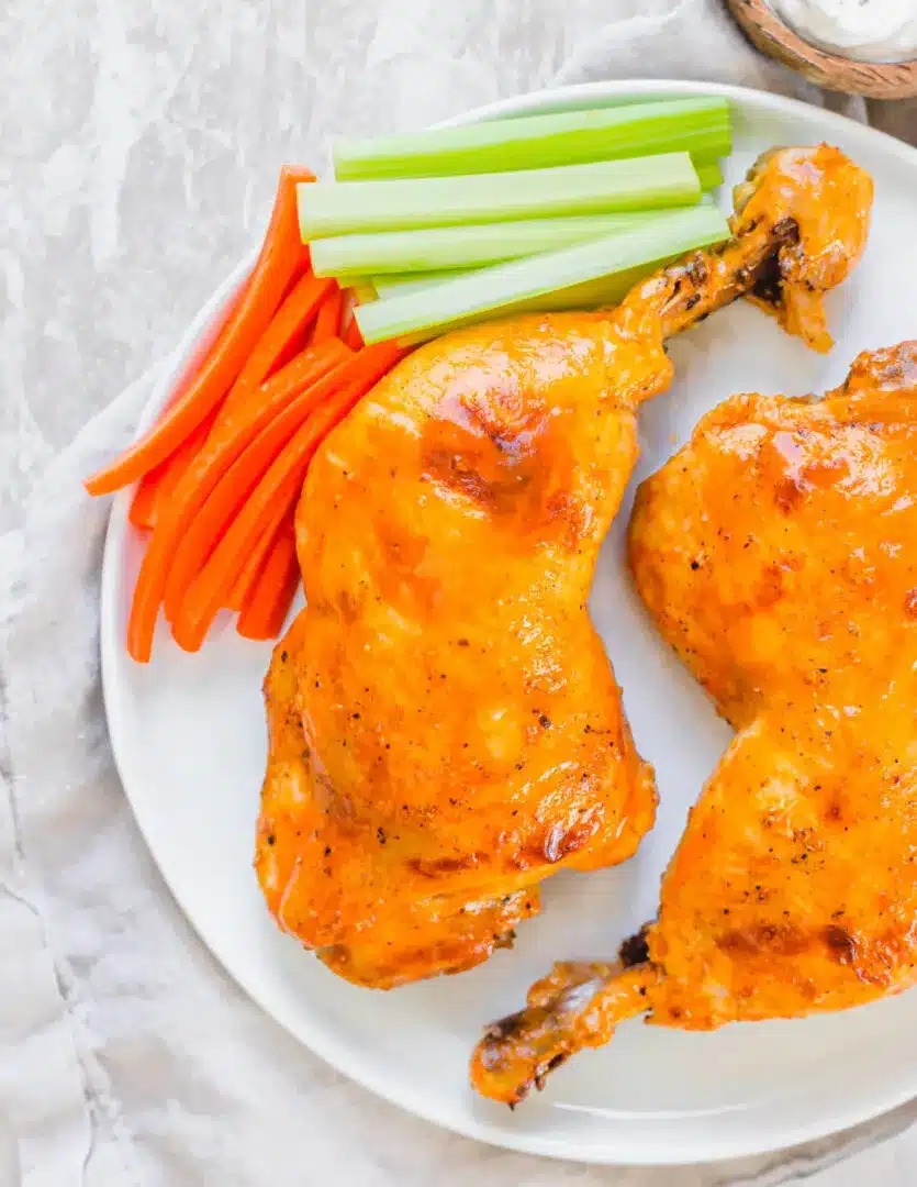 Buffalo instant pot chicken leg quarters with carrots and celery on a white plate.