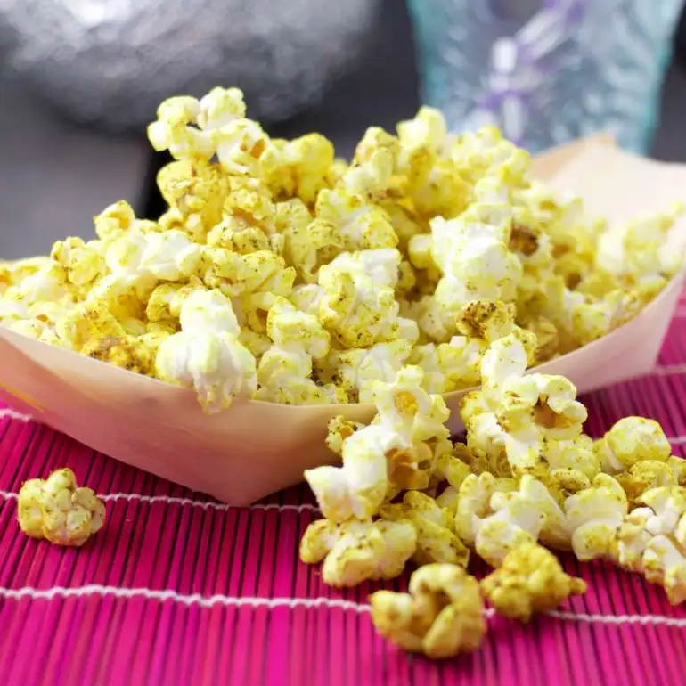 Curry popcorn in a disposable tray on a magenta placemat.