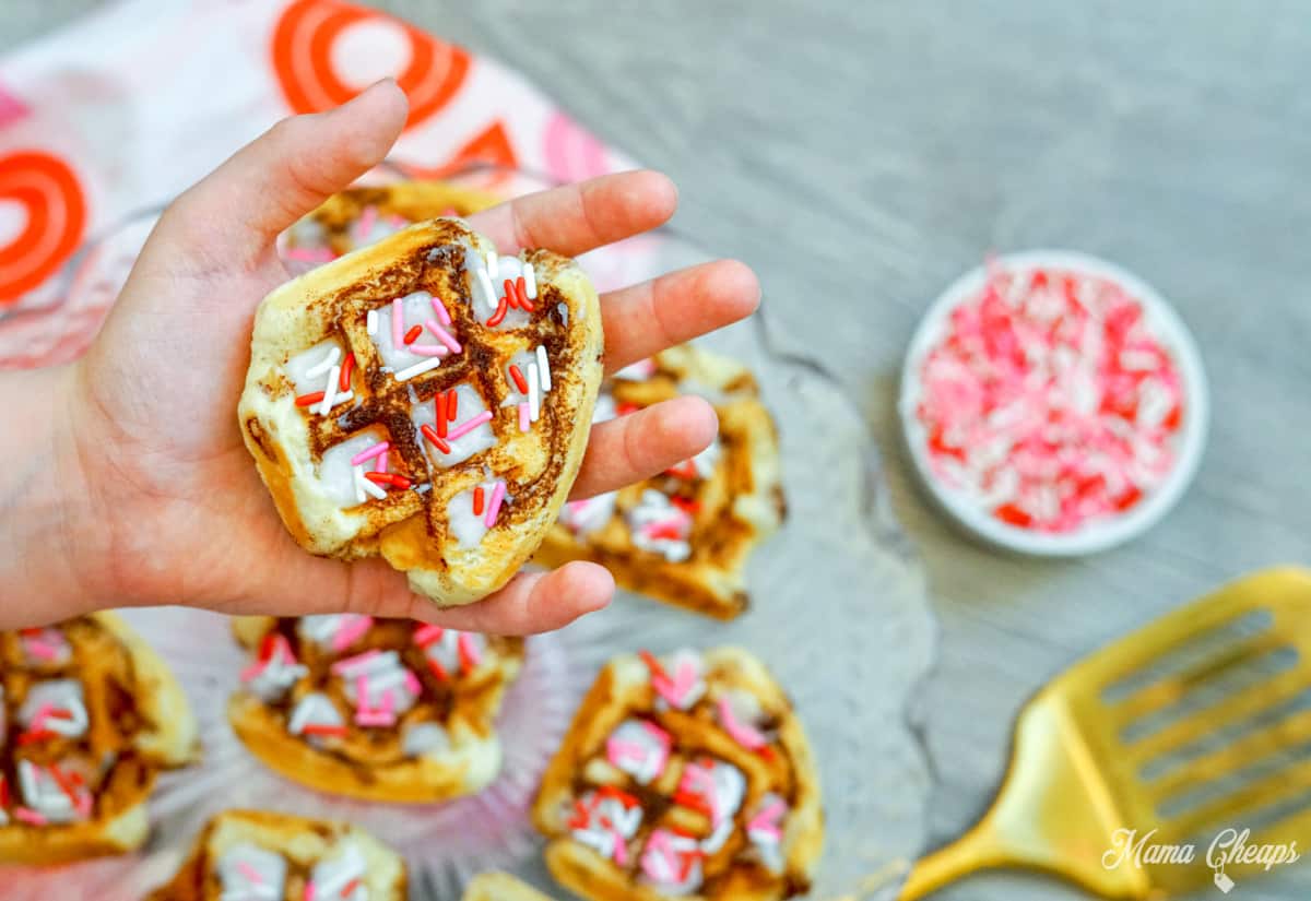 Hand holding iron cinnamon roll waffles with sprinkles.