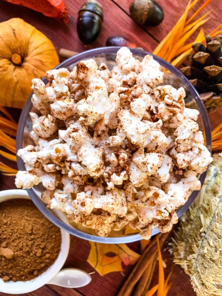 Homemade pumpkin spice popcorn in a bowl with fall adornments surrounding it.