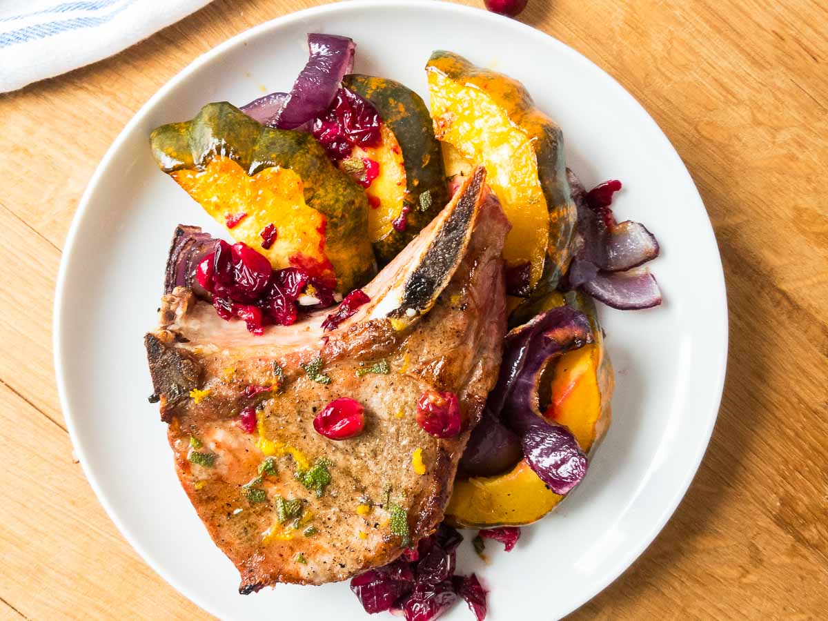 Acorn squash, cranberries, and pork chops on a white plate.