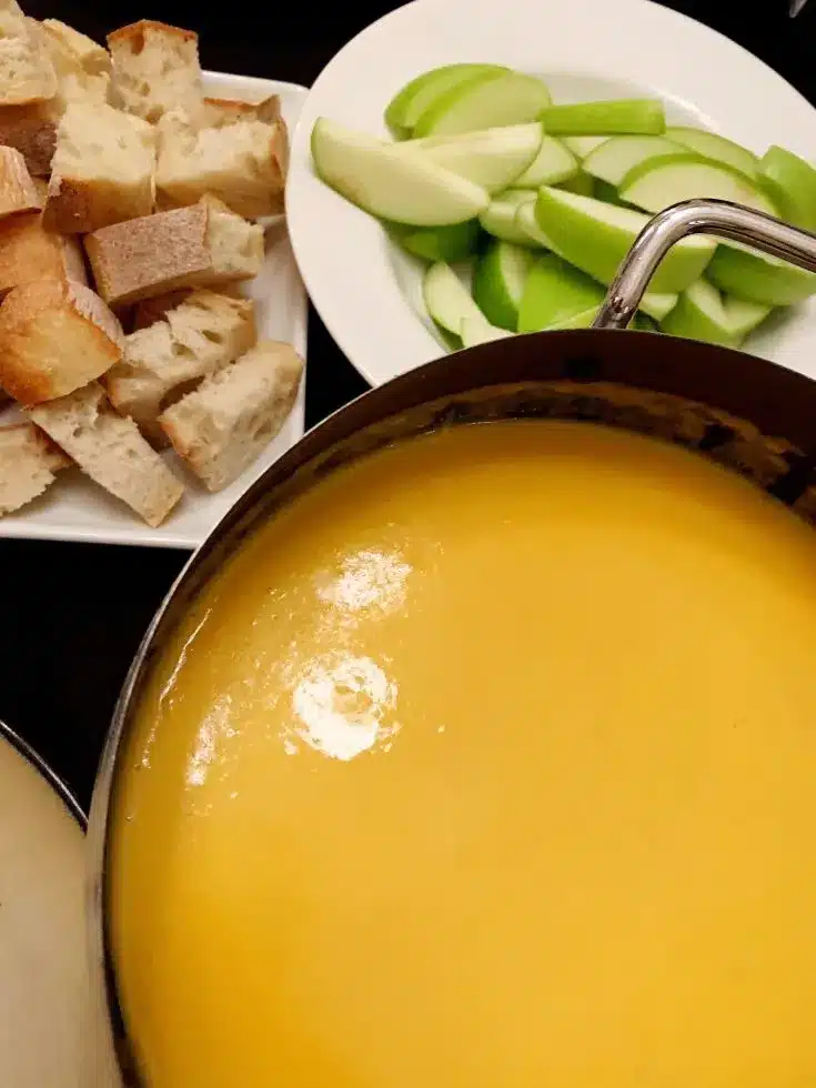 Beer cheese fondue with bread and apples in the background.