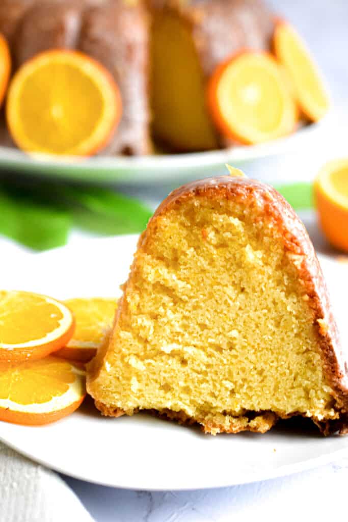 Slice of orange bundt cake on a small plate with whole cake in the background.