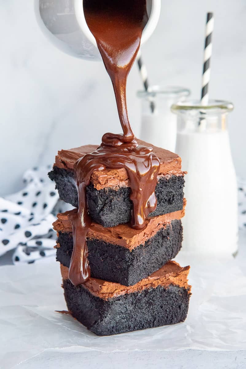 Chocolate dripping chocolate sauce on a stack of dark chocolate fudgy brownies.