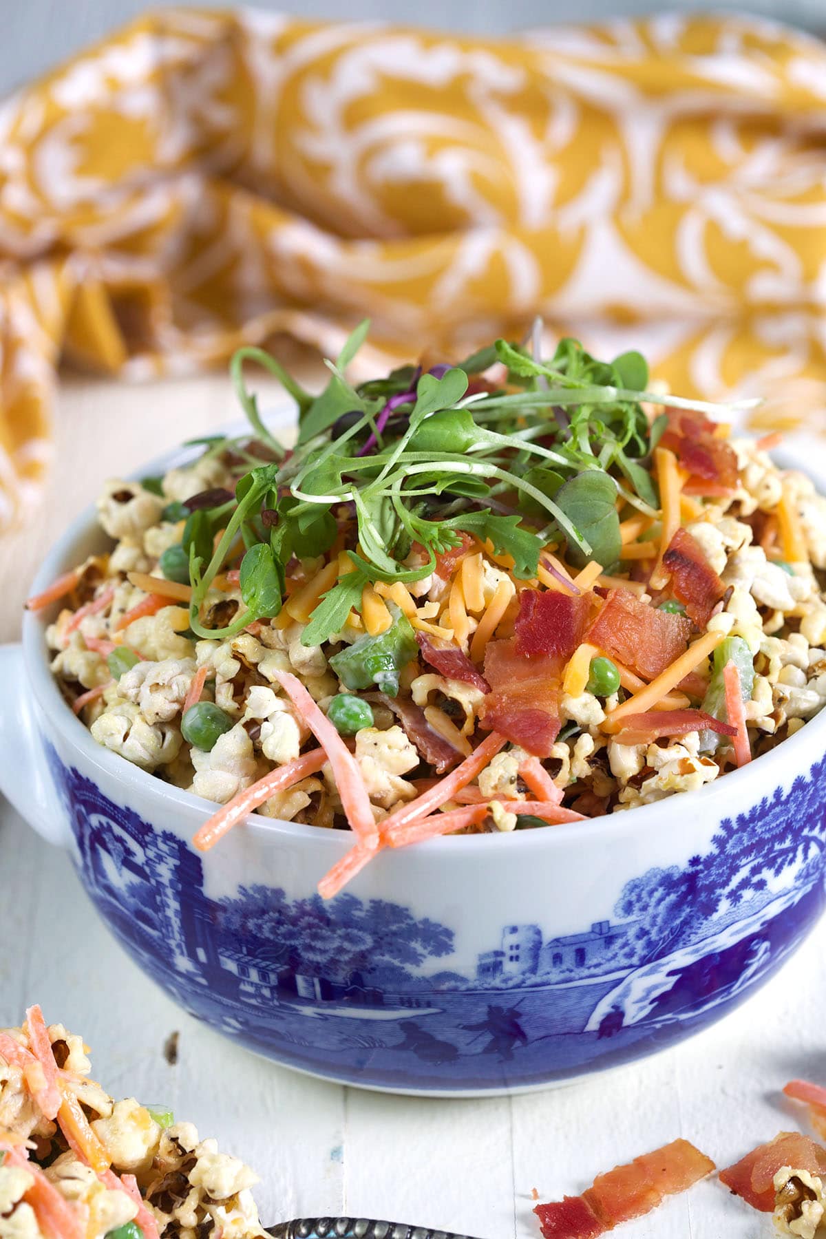 Popcorn salad with microgreens, peas, bacon, cheese, and carrots in a decorative bowl.