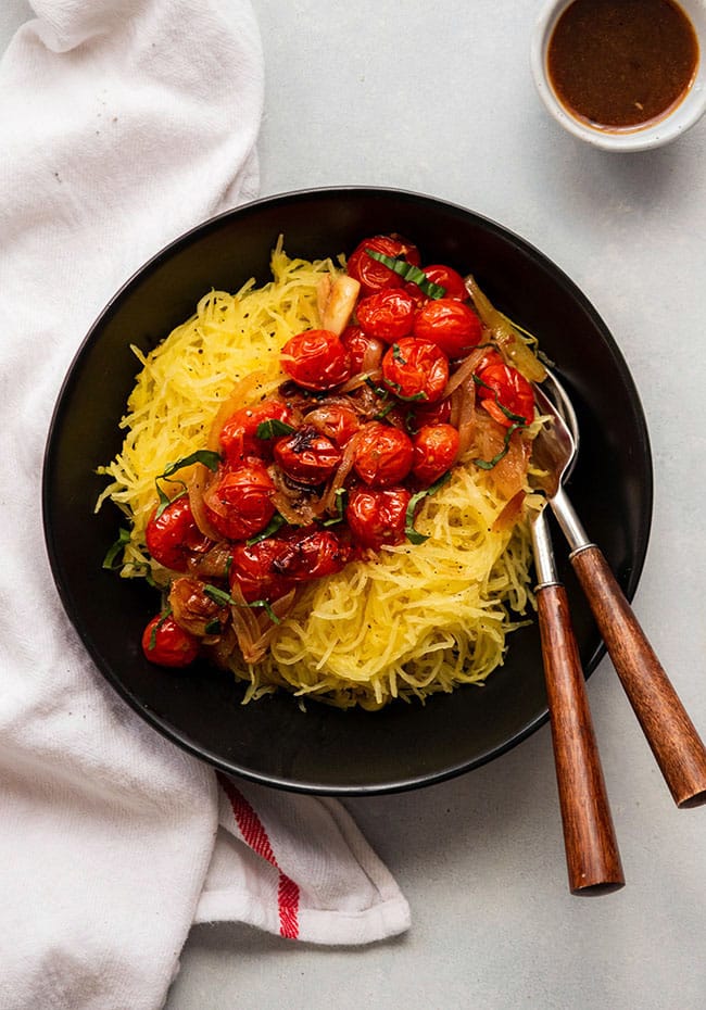 Spaghetti squash with roasted tomatoes with forks on a black plate.