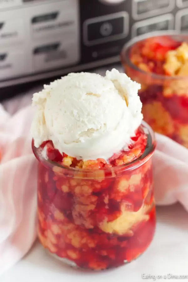 Crockpot cherry dump cake in clear glass serving dish with a scoop of vanilla ice cream on top.