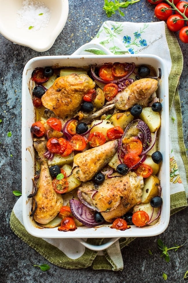 Greek chicken and roasted vegetables in a white baking dish on top of a dish towel.