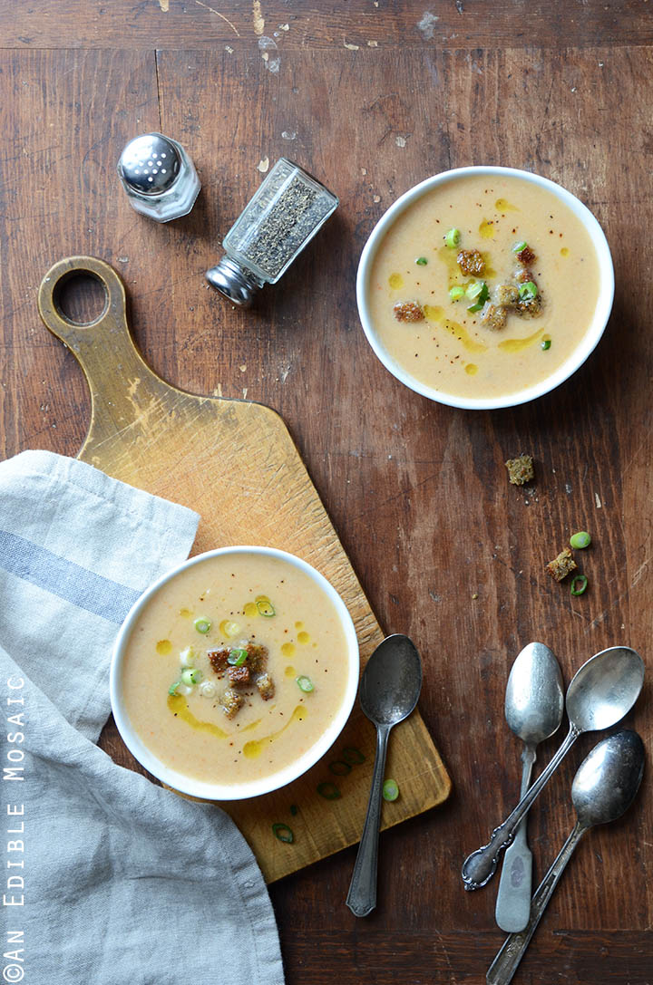 Two servings of cauliflower cheese soup with beer with spoons in the background.