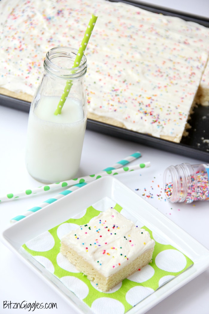 Sugar cookie cake bar on a white plate with more on a baking sheet.