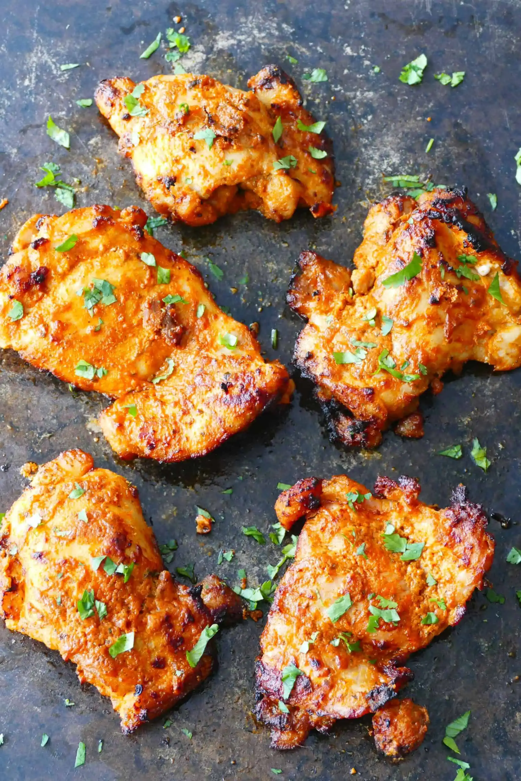 Air fryer tandoori chicken with herbs on a dark background.