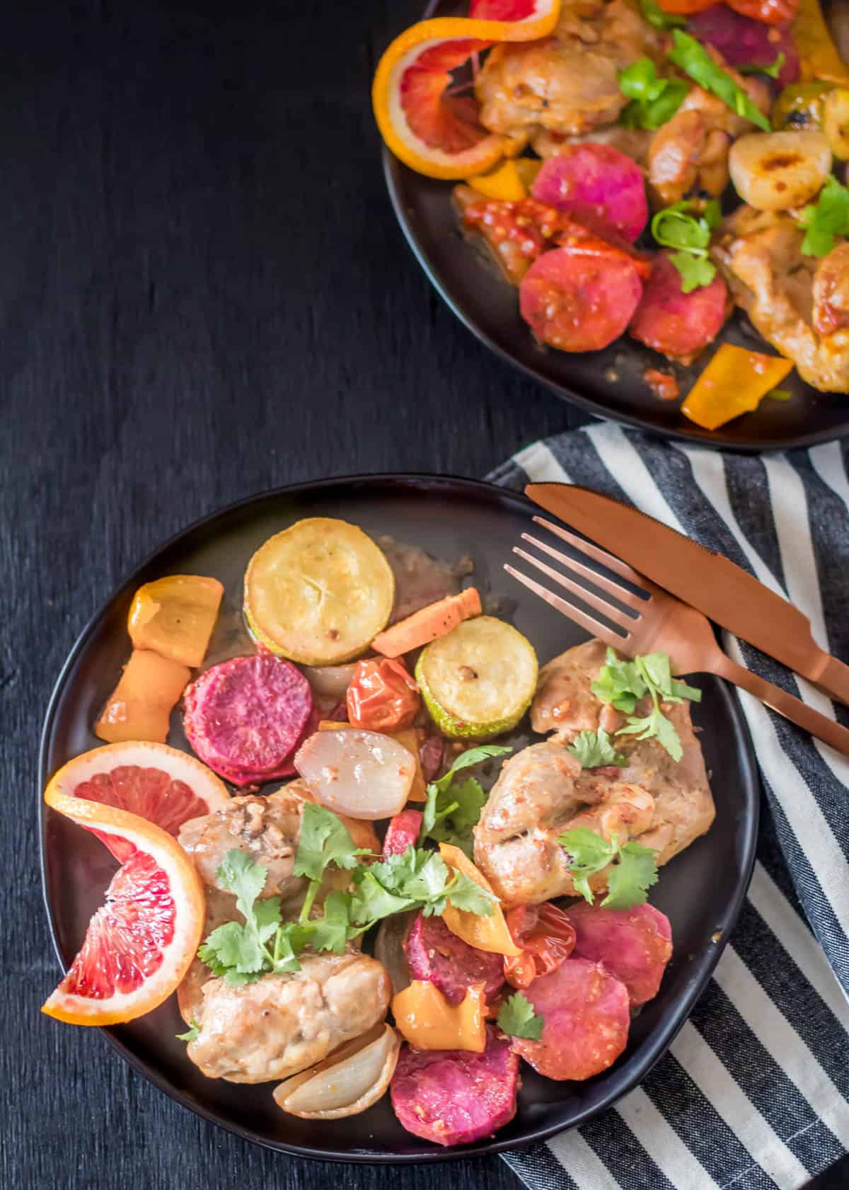 Sheet pan citrus-chipotle chicken thighs on a black plate on a black background.