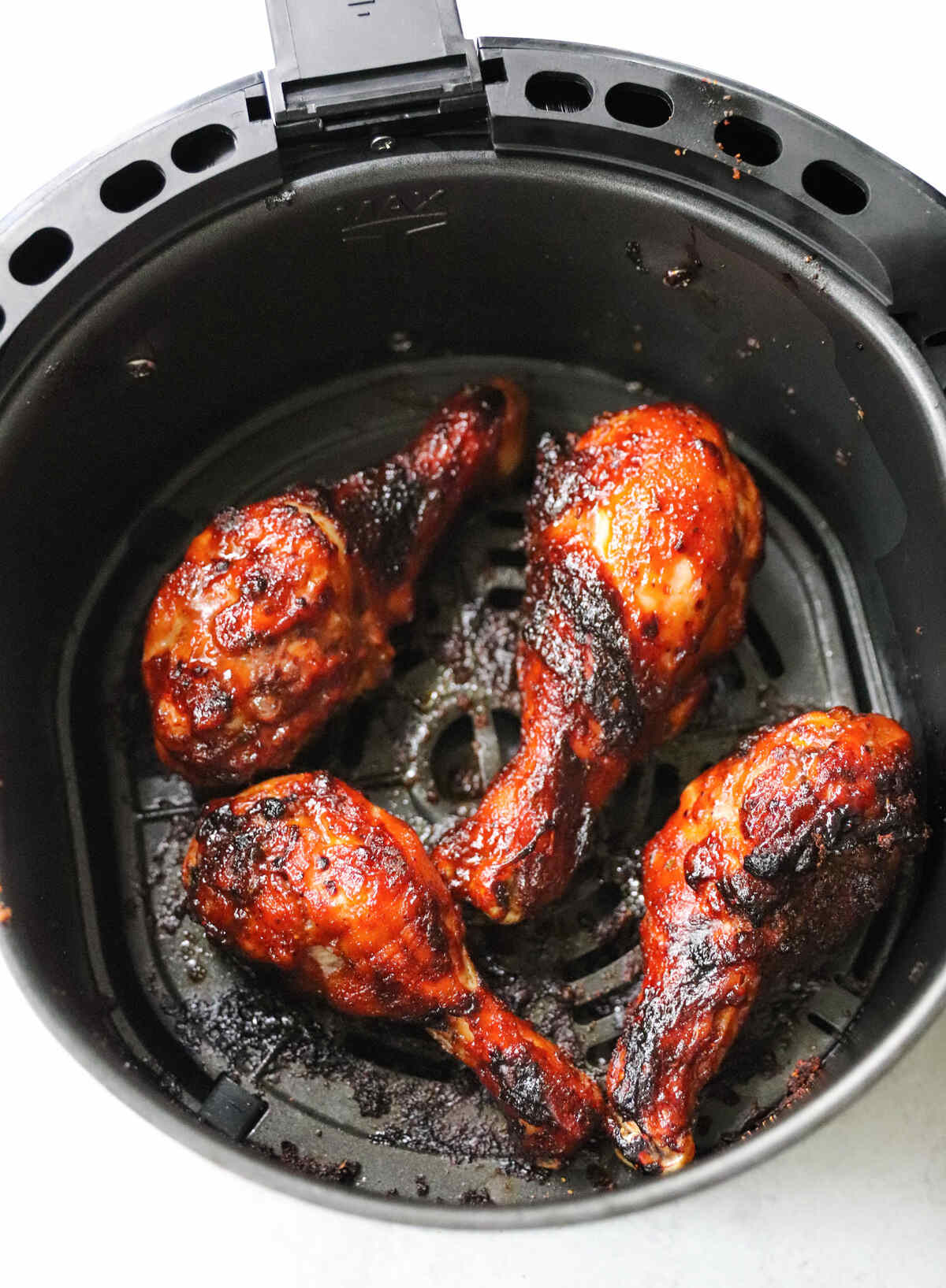 Barbecue chicken drumsticks in an air fryer basket.