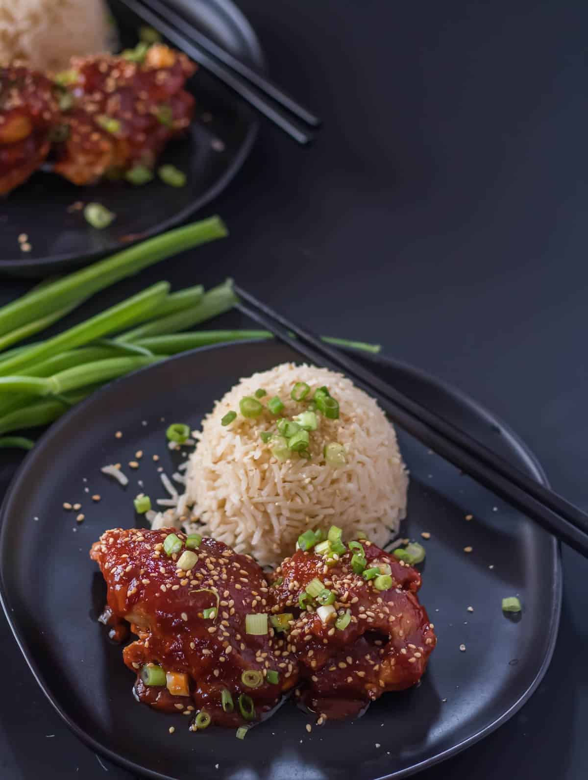 Instant pot Korean chicken thighs with rice on a dark plate.