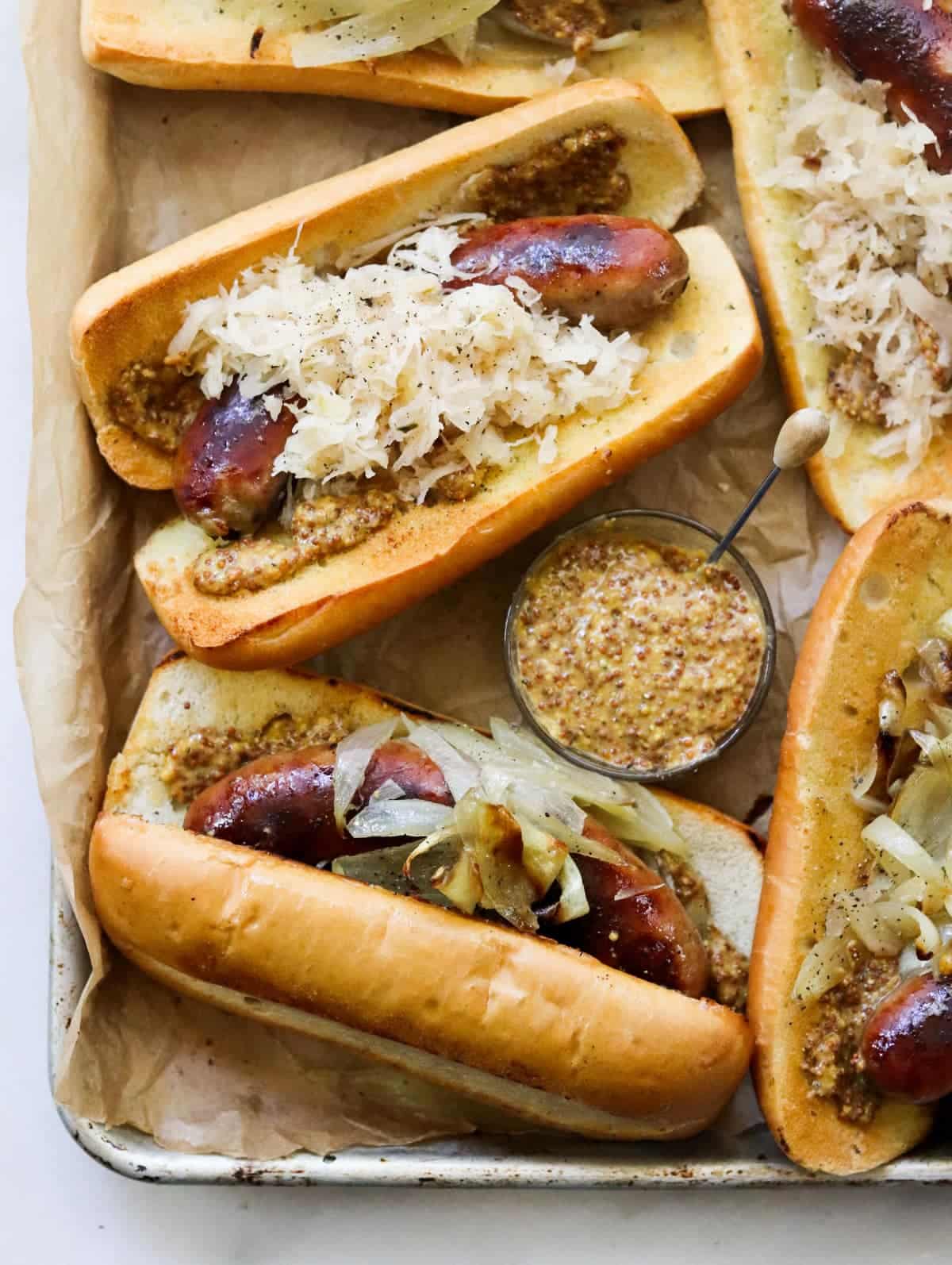 Oven baked brats with onions, sauerkraut, and mustard on a bun.