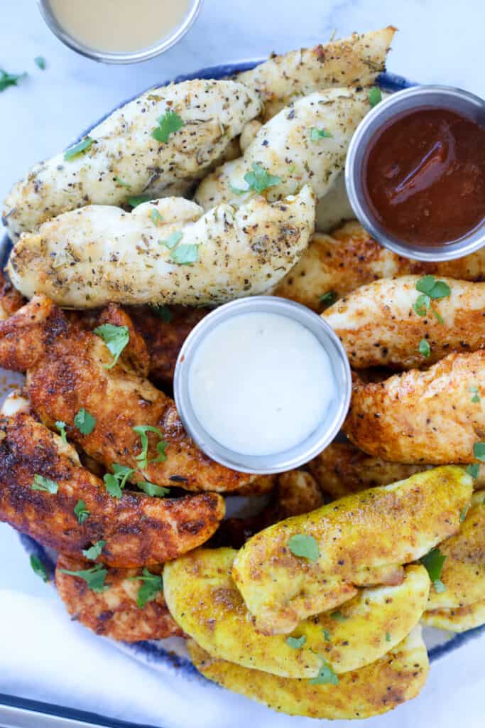 Assorted air fryer chicken tenders on a plate with sauce.