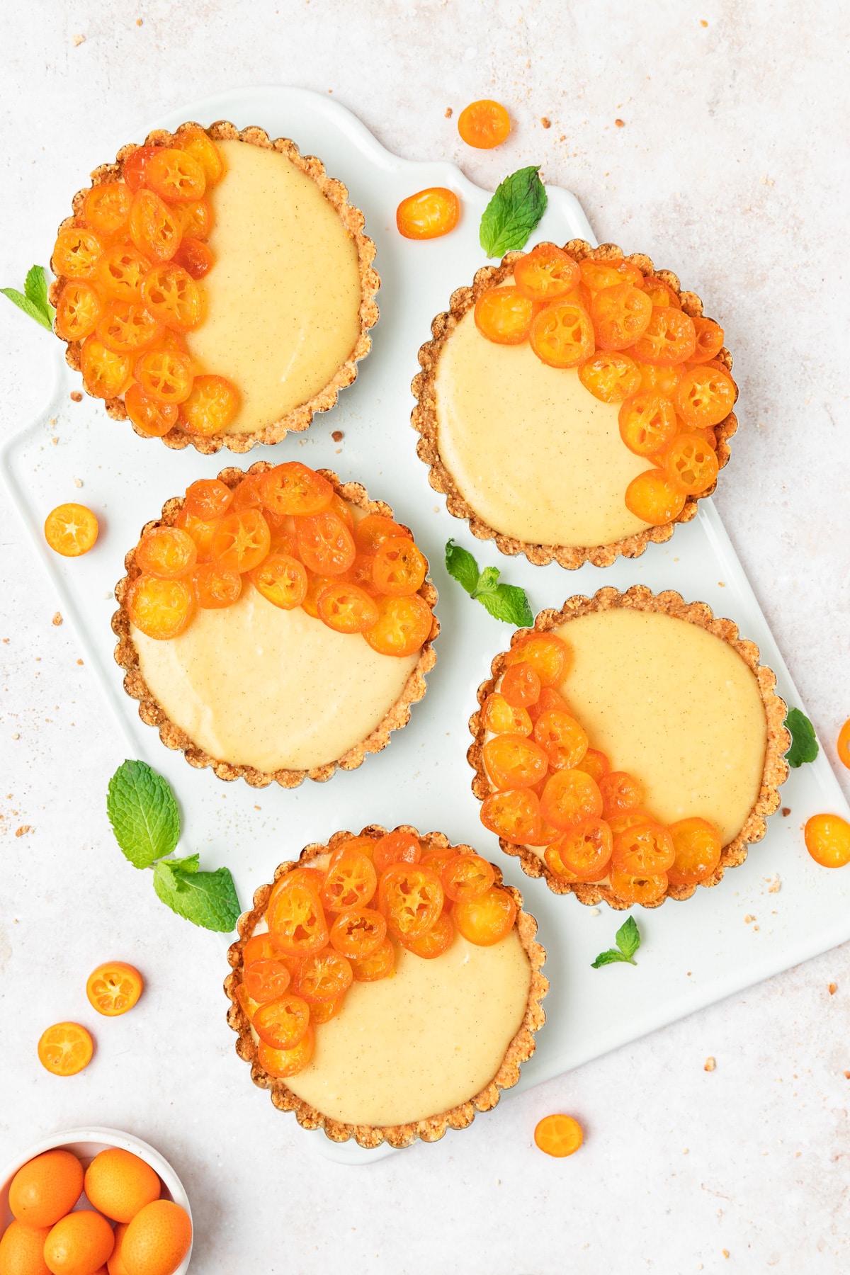 Candied kumquat and custard tarts on a white tray.