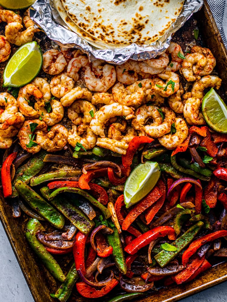 Shrimp, sliced bell peppers, lime, and tortillas in a sheet pan.