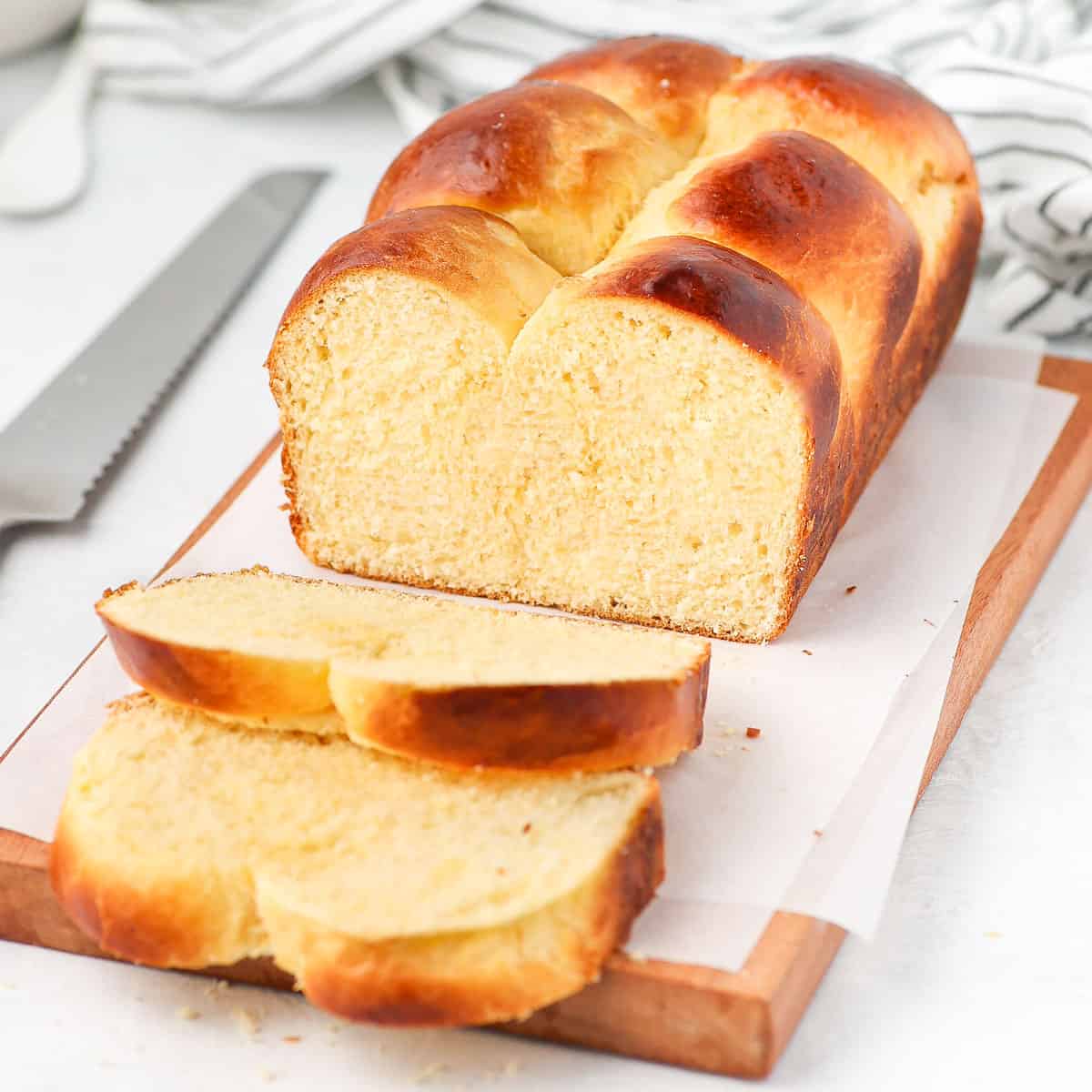 Brioche loaf bread, sliced, on a wooden cutting board with bread knife in the background.