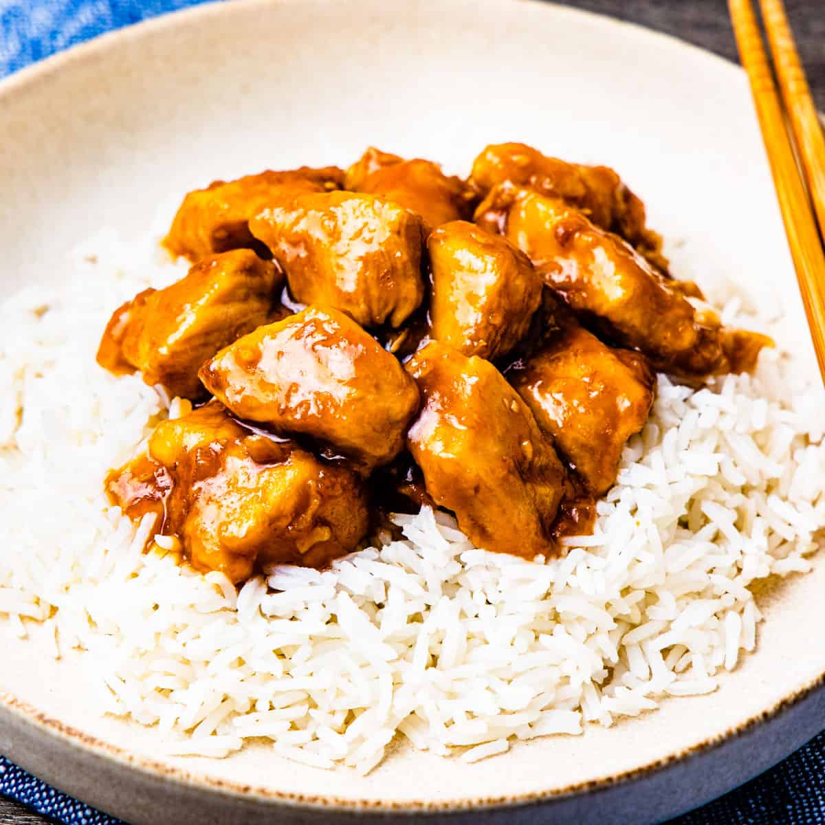 Honey bourbon chicken on top of rice on a light colored plate.